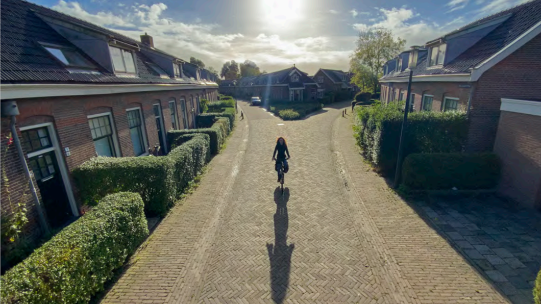 Foto van een vrouw die door de Hollanderwijk fietst met op de achtergrond de zon